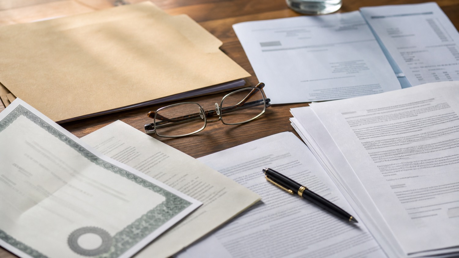 Business registration documents, a certificate and a utility bill laid out on a desk with a pen and glasses